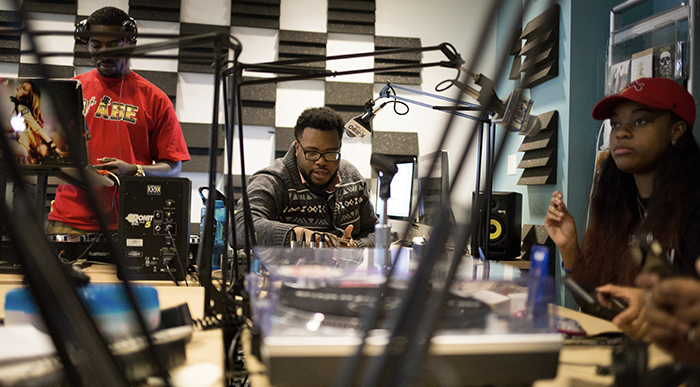 students-sit-at-a-table-with-microphones-and-other-broadcasting-equipment-at-the-student-run-radio-station