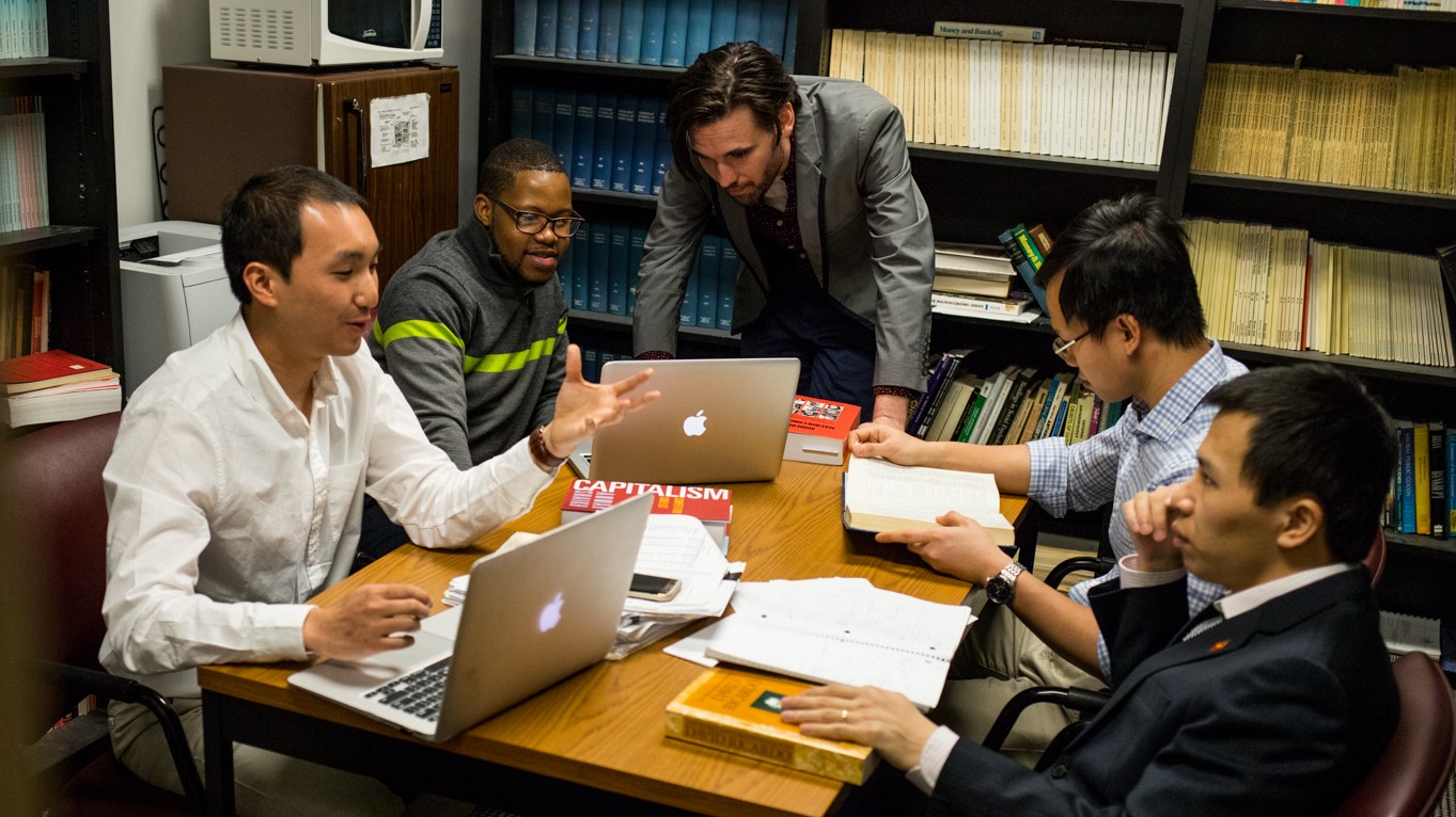 three students sit along bench with monitors in front of them in research lab